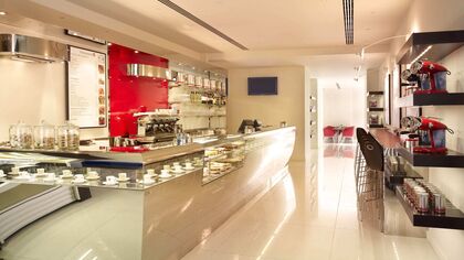 White and chrome bar counter at the illy cafe during the day with white tile floor and chrome coffee machine