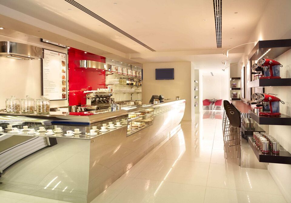 White and chrome bar counter at the illy cafe during the day with white tile floor and chrome coffee machine