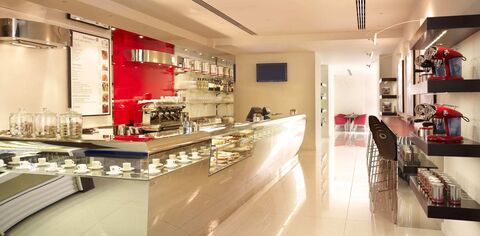White and chrome bar counter at the illy cafe during the day with white tile floor and chrome coffee machine