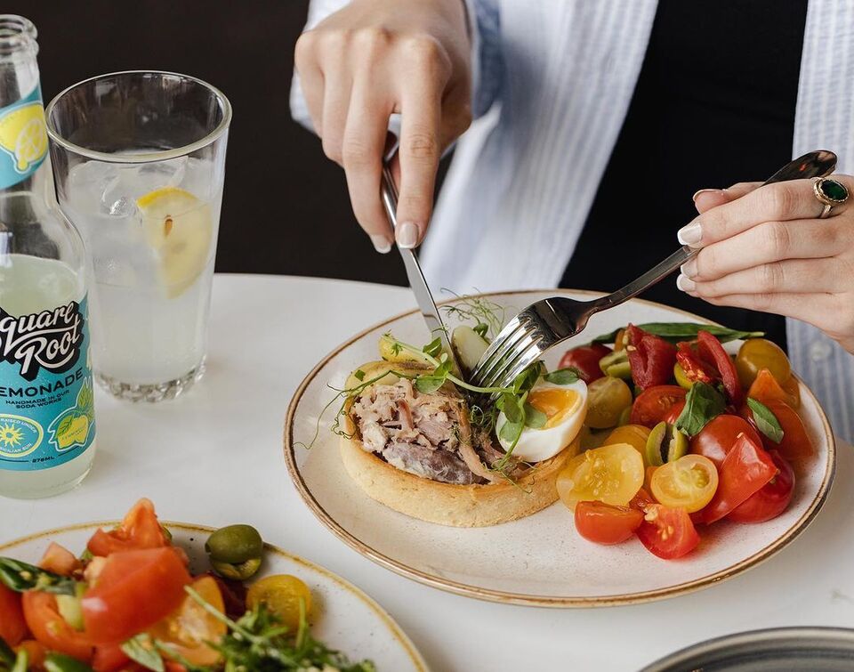 close up of a plate of quiche and a bright tomato salad with a person tucking in with knife and fork