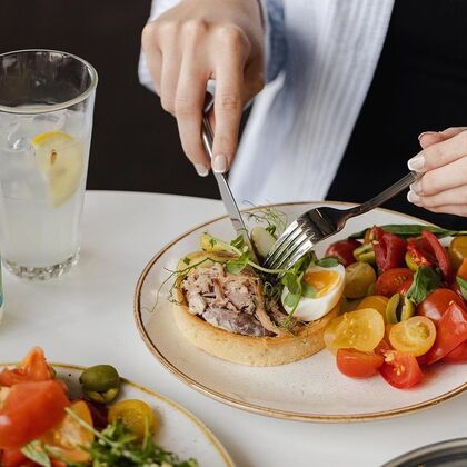 close up of a plate of quiche and a bright tomato salad with a person tucking in with knife and fork
