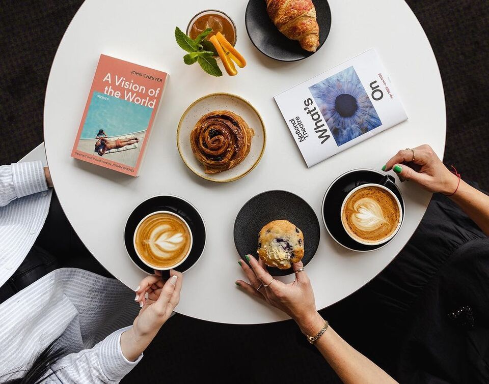 aerial view of a table with 2 cups of coffee, 2 theatre programmes, a muffin, a cinnamon roll and a croissant