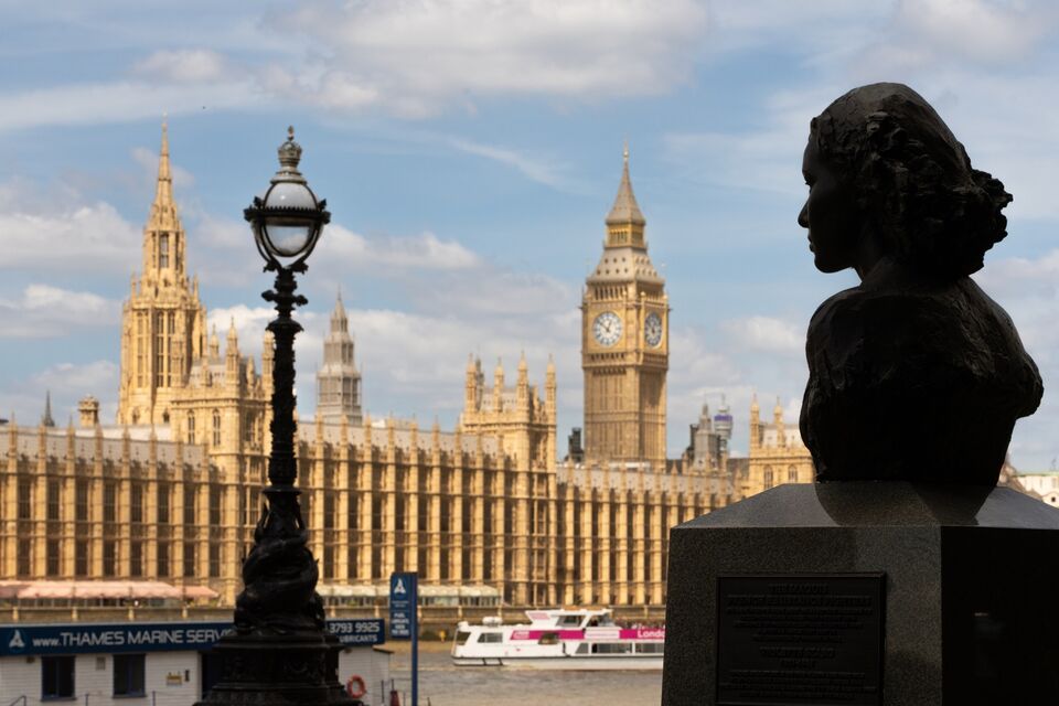 view of the house of parliament from south bank with bronze bust of a woman's head in the foreground on the right and an ornated victorian lampost on the left