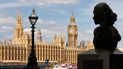 view of the house of parliament from south bank with bronze bust of a woman's head in the foreground on the right and an ornated victorian lampost on the left