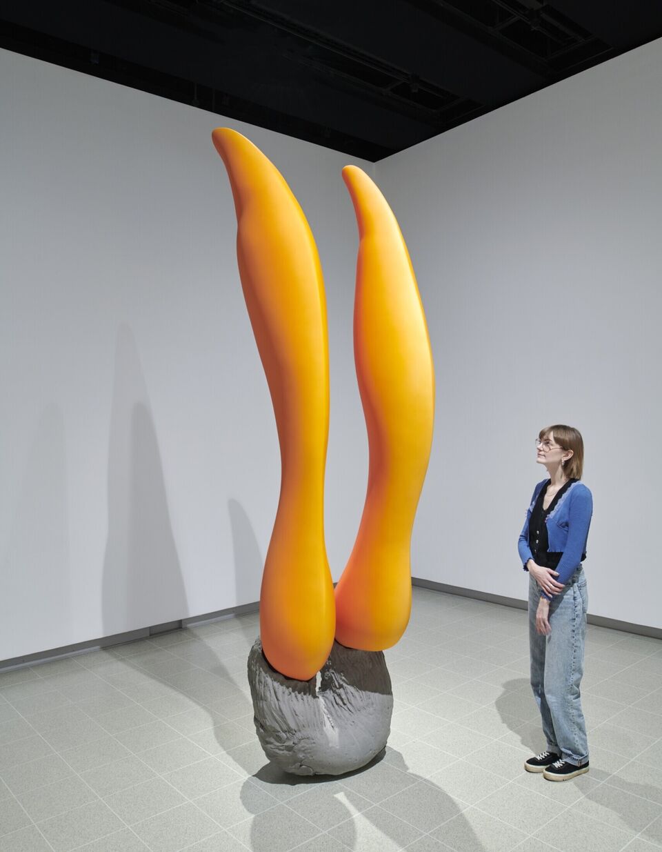 A woman looks at a tall orange and grey art installation  in a gallery