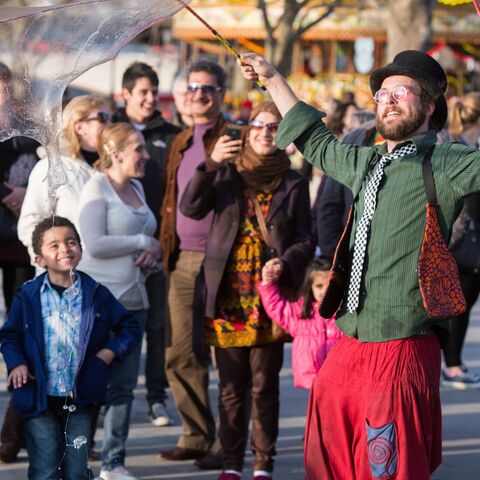 A street performer creates huge soap bubbles being watched by smiling small children