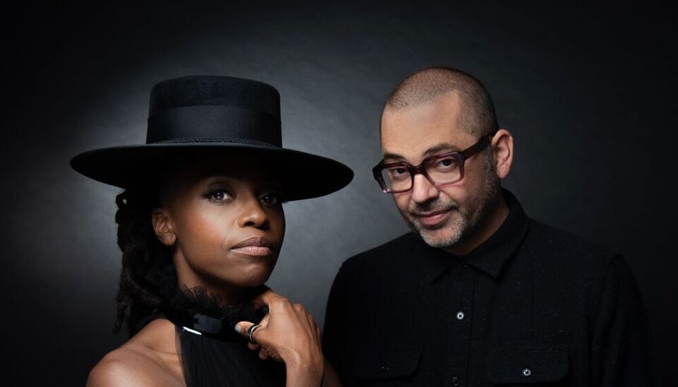 Two members of Morcheeba against a black background wearing black clothes, one person in a hat.