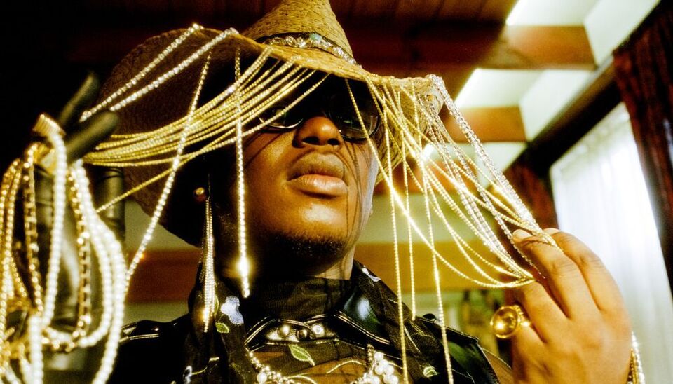 Artist SIPHO. wearing a cowboy hat with strings of rhinestones hanging from the brim, sunglasses, a black leather jacket and opulent beaded necklace.