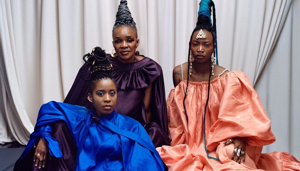 Three members of the band Les Amazones D'Afrique wearing long colourful dresses and African jewellery and hairstyles.