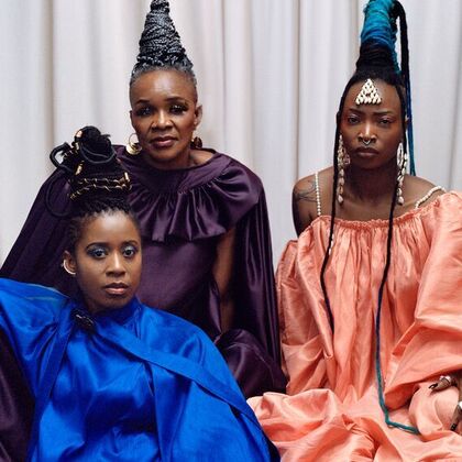Three members of the band Les Amazones D'Afrique wearing long colourful dresses and African jewellery and hairstyles.