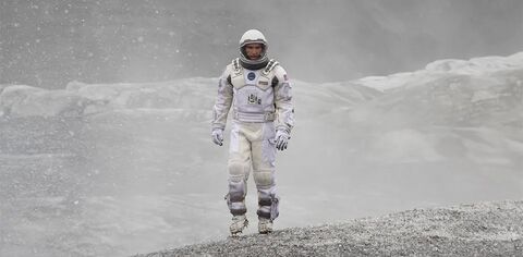 An astronaut walks alone across a grey snowy planet