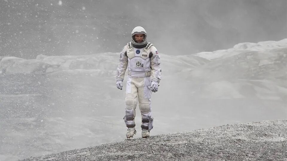 An astronaut walks alone across a grey snowy planet
