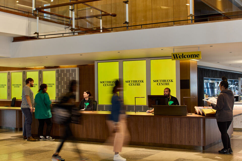 People walk up to a ticket desk where there is a sign saying welcome and a yellow background that says southbank centre