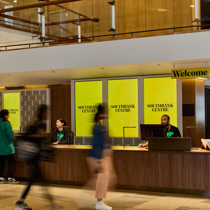 People walk up to a ticket desk where there is a sign saying welcome and a yellow background that says southbank centre