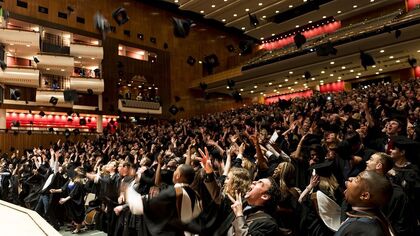 Concert Hall full of graduates in formal gowns throwing hats