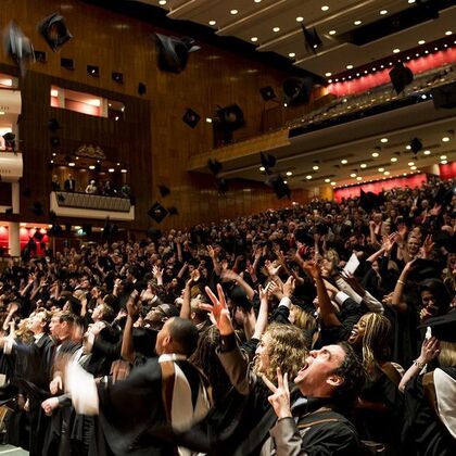 Concert Hall full of graduates in formal gowns throwing hats