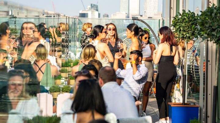 People enjoying drinks on a sunny day on a rooftop with London skyscrapers in the background