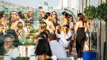 People enjoying drinks on a sunny day on a rooftop with London skyscrapers in the background