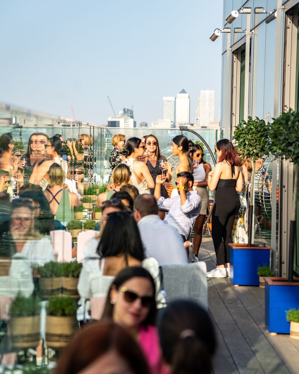 People enjoying drinks on a sunny day on a rooftop with London skyscrapers in the background