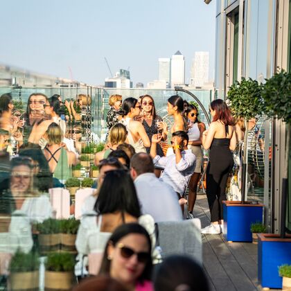 People enjoying drinks on a sunny day on a rooftop with London skyscrapers in the background