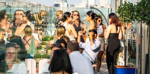 People enjoying drinks on a sunny day on a rooftop with London skyscrapers in the background