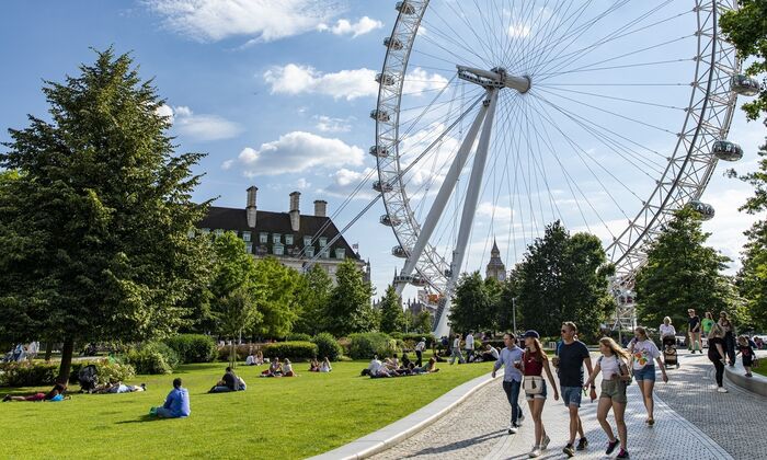 Tourists walk through Jubilee Gardens in the summer with the Lonon Eye and Big Ben in the background