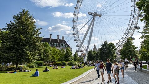 Tourists walk through Jubilee Gardens in the summer with the Lonon Eye and Big Ben in the background