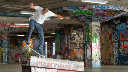 A skater practices a flip in a concrete undercroft covered that is covered in graffiti tags