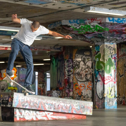 A skater practices a flip in a concrete undercroft covered that is covered in graffiti tags