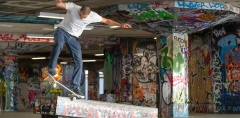 A skater practices a flip in a concrete undercroft covered that is covered in graffiti tags