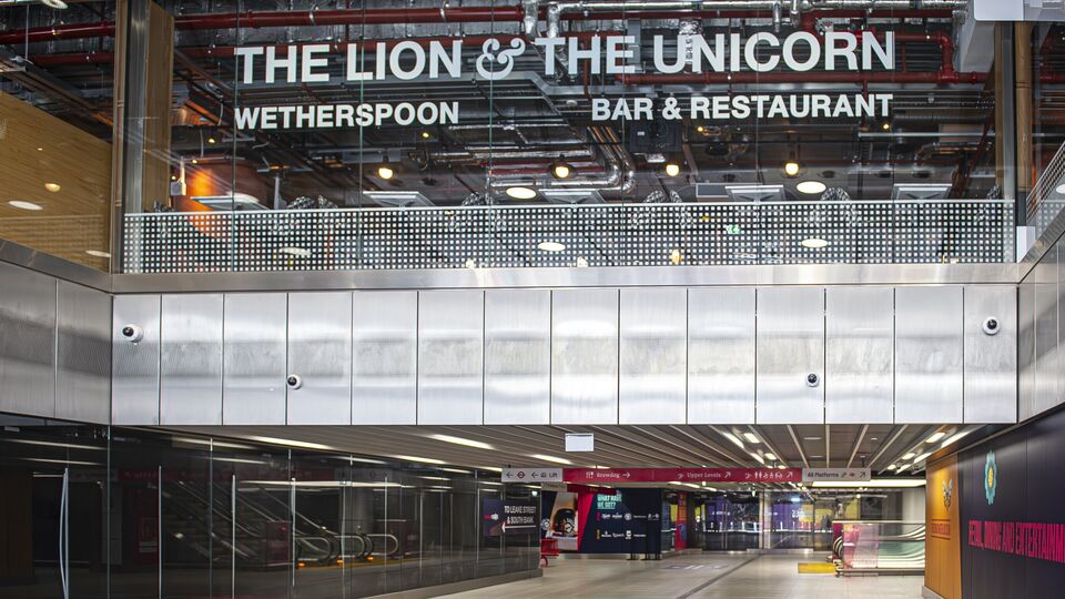 The Lion and Unicorn signage on a large window overlooking train station escalators