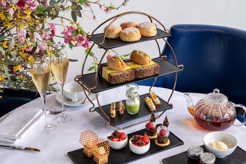 Afternoon tea stand with cakes and sandwiches, pot of tea and two glasses of champagne